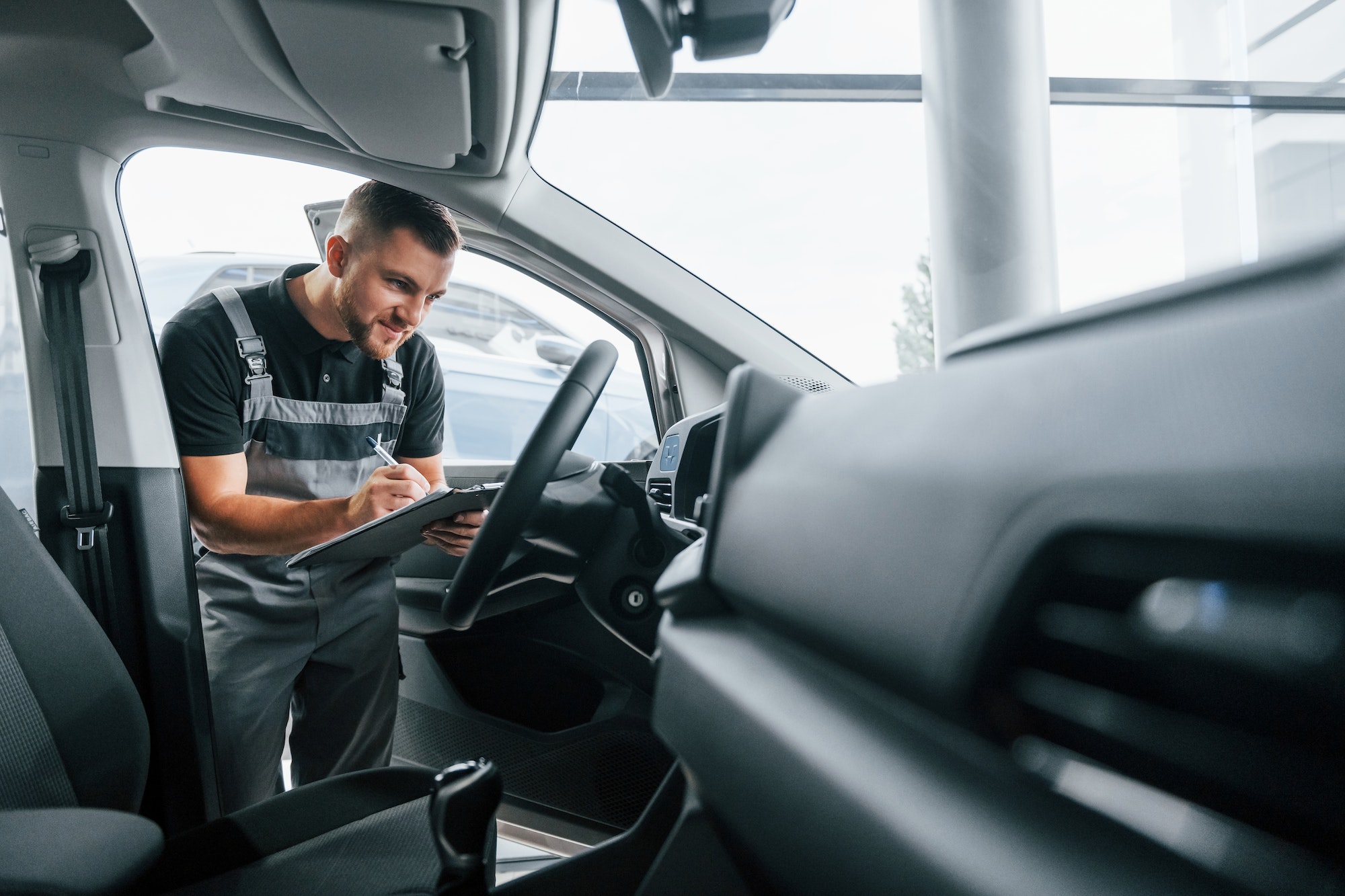 Looking inside the car. Man in uniform is working in the autosalon at daytime