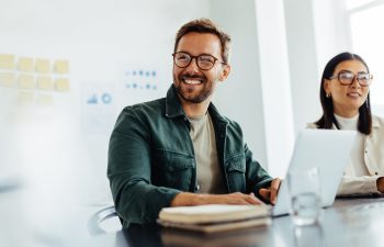 smiling man sitting behind a laptop in a conference room